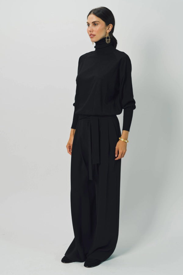 Front slanted view of black ls t-neck raglan sweater on model wearing black pants, against a white background.