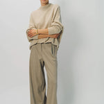 Front view of sand cashmere light full pants on model wearing oatmeal sweater, against a white background.