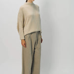 Side view of sand cashmere light full pants on model wearing oatmeal sweater, against a white background.