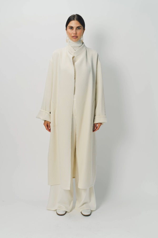 Front view of ivory long cardigan coat on model wearing white turtleneck and pants, against a white background.