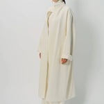 Front slanted view of ivory long cardigan coat on model wearing white pants and turtleneck, against a white background.