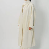 Front slanted view of ivory long cardigan coat on model wearing white pants and turtleneck, against a white background.