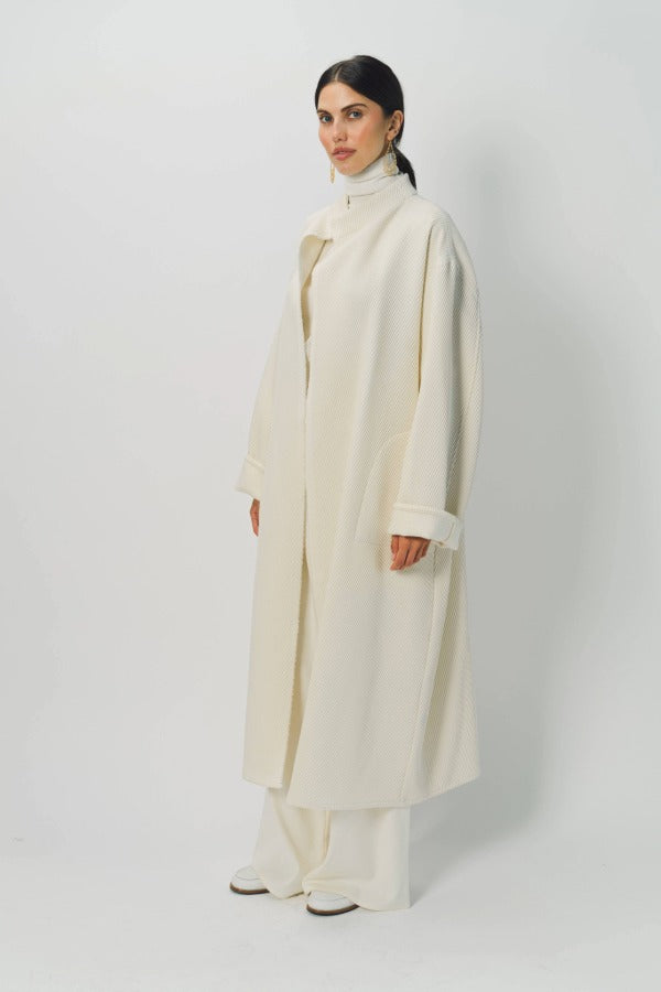 Front slanted view of ivory long cardigan coat on model wearing white pants and turtleneck, against a white background.