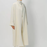 Front slanted view of ivory long cardigan coat on model wearing white pants and turtleneck, against a white background.