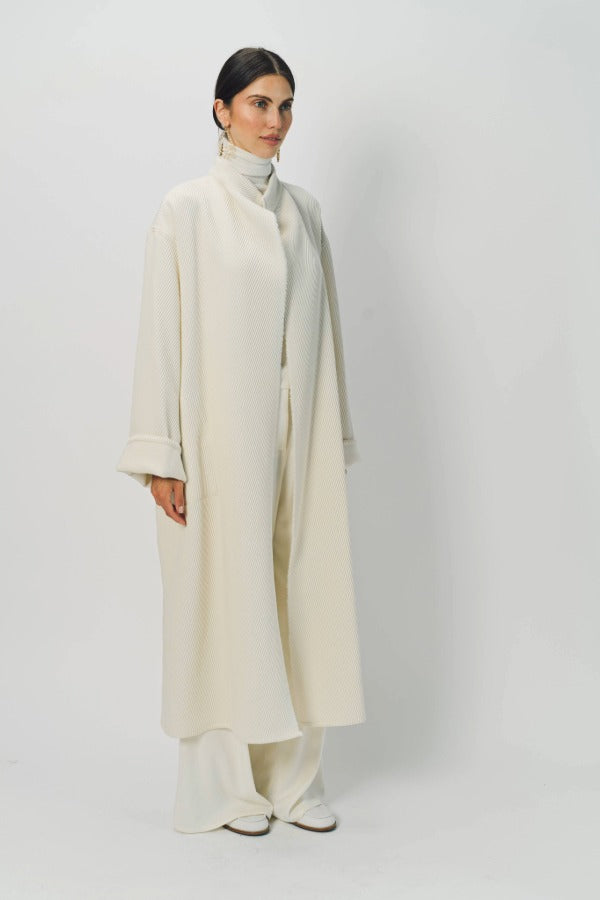 Front slanted view of ivory long cardigan coat on model wearing white pants and turtleneck, against a white background.