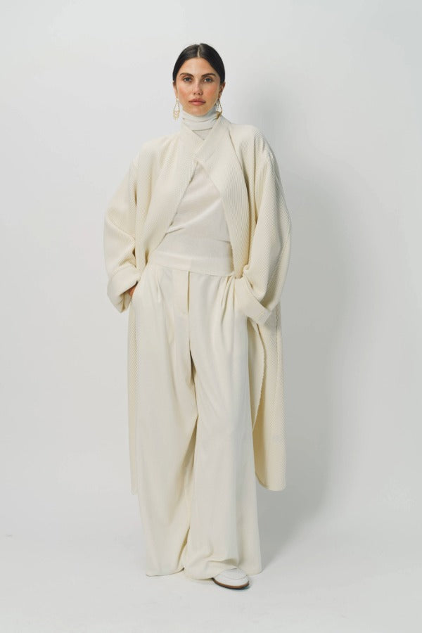 Alternate front view of ivory long cardigan coat on model wearing white pants and turtleneck, against a white background.