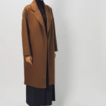 Side view of palissandro oversized coat on model wearing navy turtleneck, pants and loafers, against a white background.