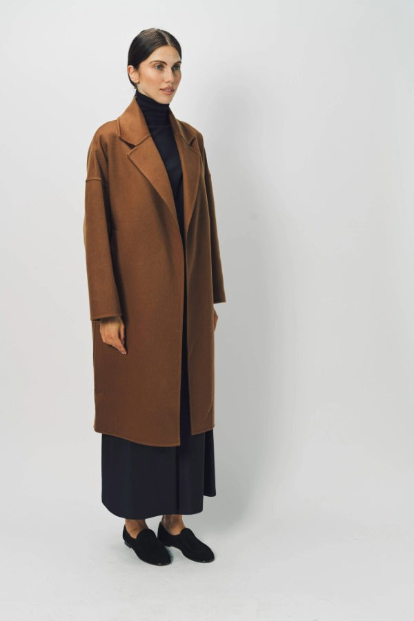 Side view of palissandro oversized coat on model wearing navy turtleneck, pants and loafers, against a white background.