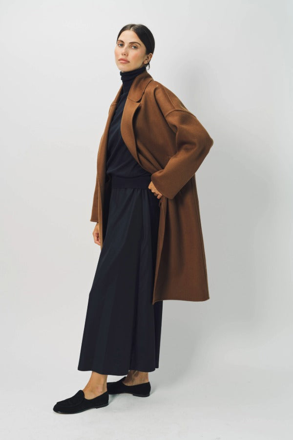 Alternate side view of palissandro oversize coat on model wearing navy turtleneck, pants and loafers, against a white background.