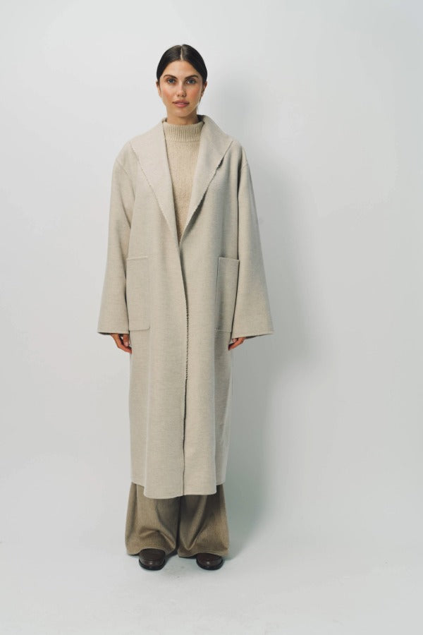 Front view of oatmeal cashmere patch pocket long coat on model wearing beige pants and oatmeal sweater, against a white background.