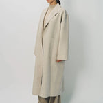Side view of oatmeal cashmere patch pocket long coat on model wearing beige pants and oatmeal sweater, against a white background.