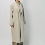 Front slanted view of oatmeal patch pocket long coat on model wearing beige pants and oatmeal sweater, against a white background.