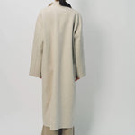 Back view of oatmeal cashmere patch pocket long coat on model wearing beige pants , against a white background.
