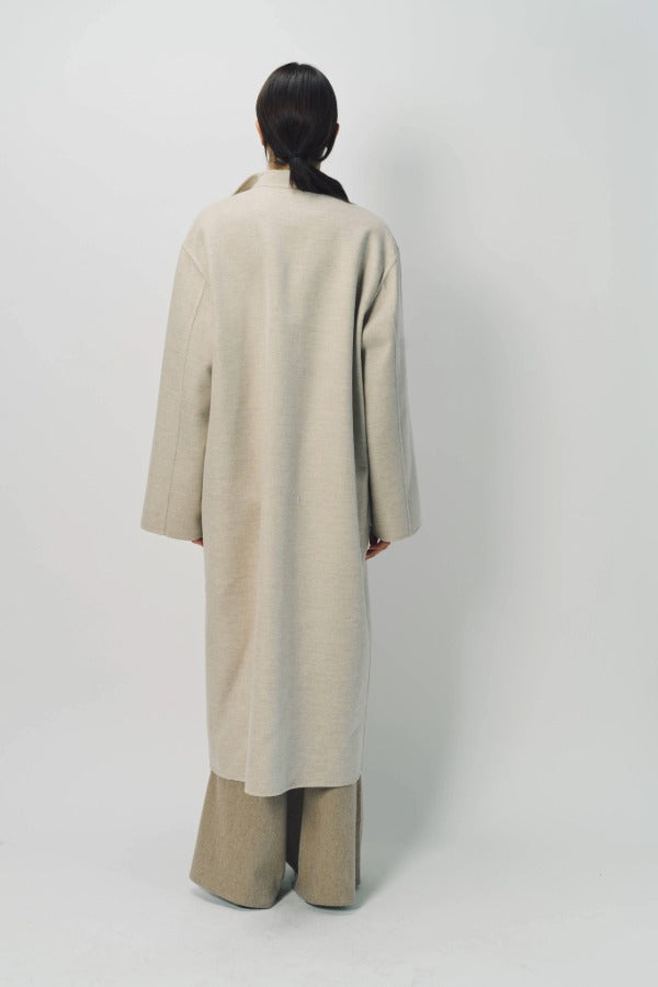 Back view of oatmeal cashmere patch pocket long coat on model wearing beige pants , against a white background.