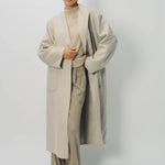 Alternate front view of oatmeal cashmere patch pocket long coat on model wearing beige pants and oatmeal sweater, against a white background.