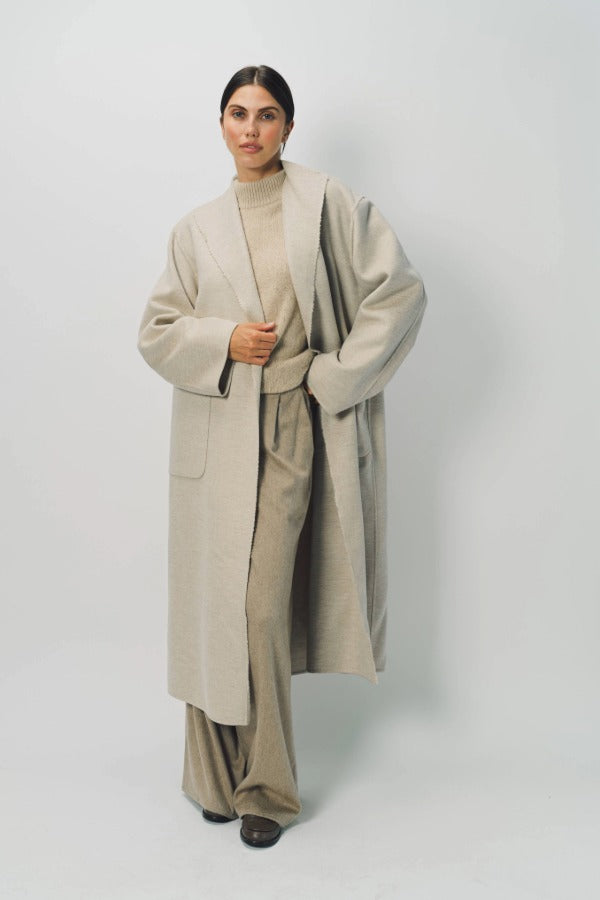 Alternate front view of oatmeal cashmere patch pocket long coat on model wearing beige pants and oatmeal sweater, against a white background.