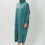 Side view of norfolk blue iconic cashmere t-neck dress on model wearing loafers, against a white background.