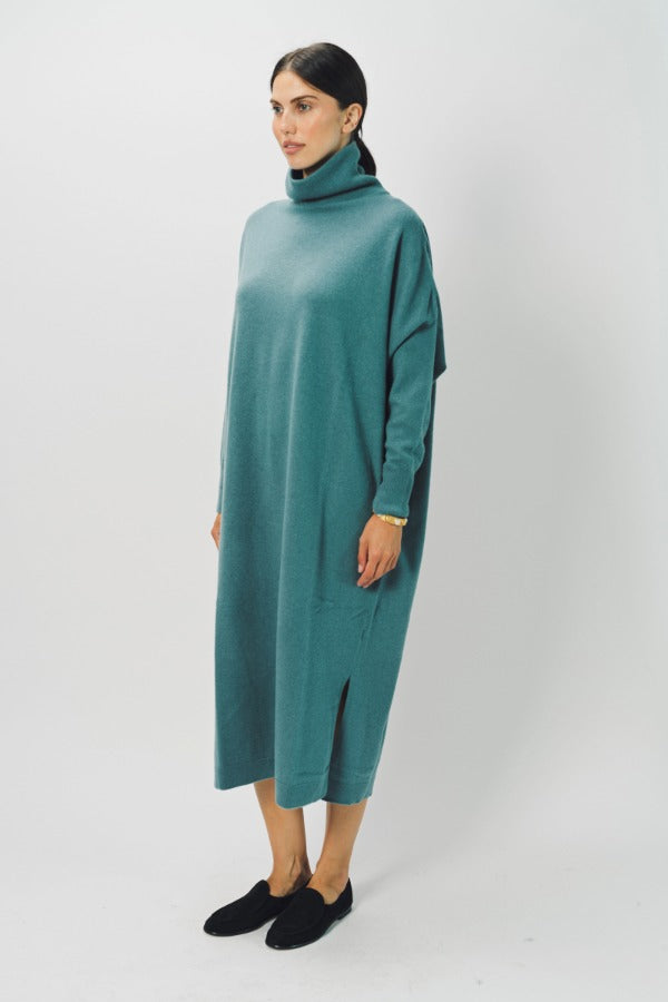 Side view of norfolk blue iconic cashmere t-neck dress on model wearing loafers, against a white background.