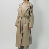 Side view of sand light cashmere trench coat on model wearing sand pants and sweater, against a white background.