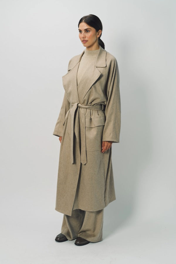 Side view of sand light cashmere trench coat on model wearing sand pants and sweater, against a white background.