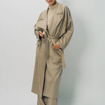 Alternate front view of sand light cashmere trench coat on model wearing sand pants and sweater, against a white background.