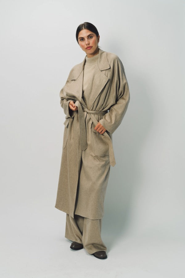 Alternate front view of sand light cashmere trench coat on model wearing sand pants and sweater, against a white background.