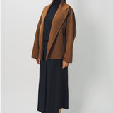 Side view of palissandro oversized coat on model wearing black top, pants and loafers, against a white background.