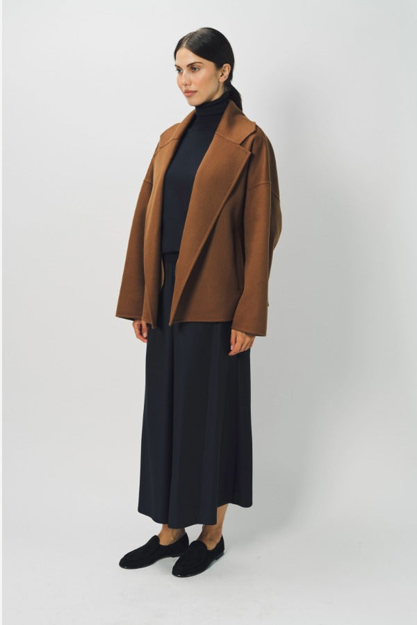 Side view of palissandro oversized coat on model wearing black top, pants and loafers, against a white background.