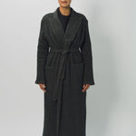 Front view of brown long cashmere jersey coat on model wearing black shirt and loafers, against a white background.