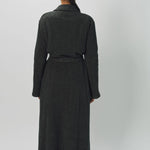 Back view of brown long cashmere jersey coat on model wearing black shirt and loafers, against a white background.