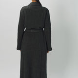 Back view of brown long cashmere jersey coat on model wearing black shirt and loafers, against a white background.