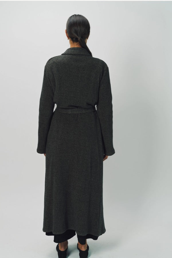 Back view of brown long cashmere jersey coat on model wearing black shirt and loafers, against a white background.