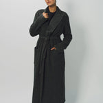 Alternate front view of brown long cashmere jersey coat on model wearing black shirt and loafers, against a white background.