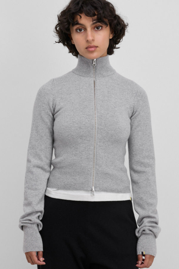 Front view of full zip grey sweater on model wearing white t-shirt and black pants, against a white background.