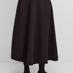 Front view of dark brown no 388 ease skirt on model wearing grey sweater and brown mary janes, against a white background.