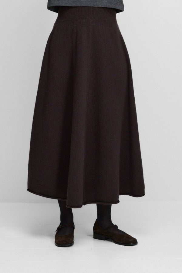 Front view of dark brown no 388 ease skirt on model wearing grey sweater and brown mary janes, against a white background.