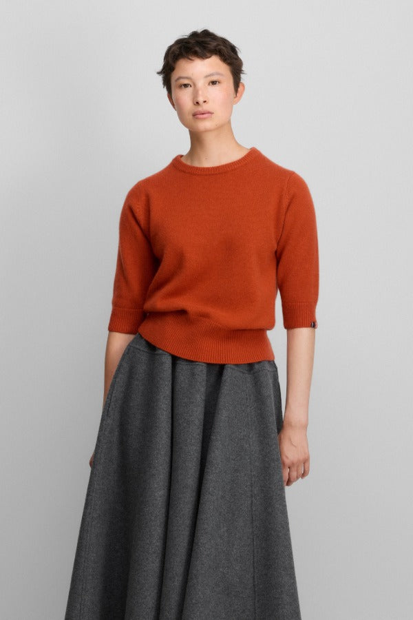 Front view of dark orange no 432 well lamb sweater on model wearing grey skirt, against a white background.