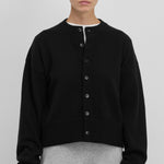 Front view of button down black cardigan on model wearing white t-shirt and grey skirt, against a white background.