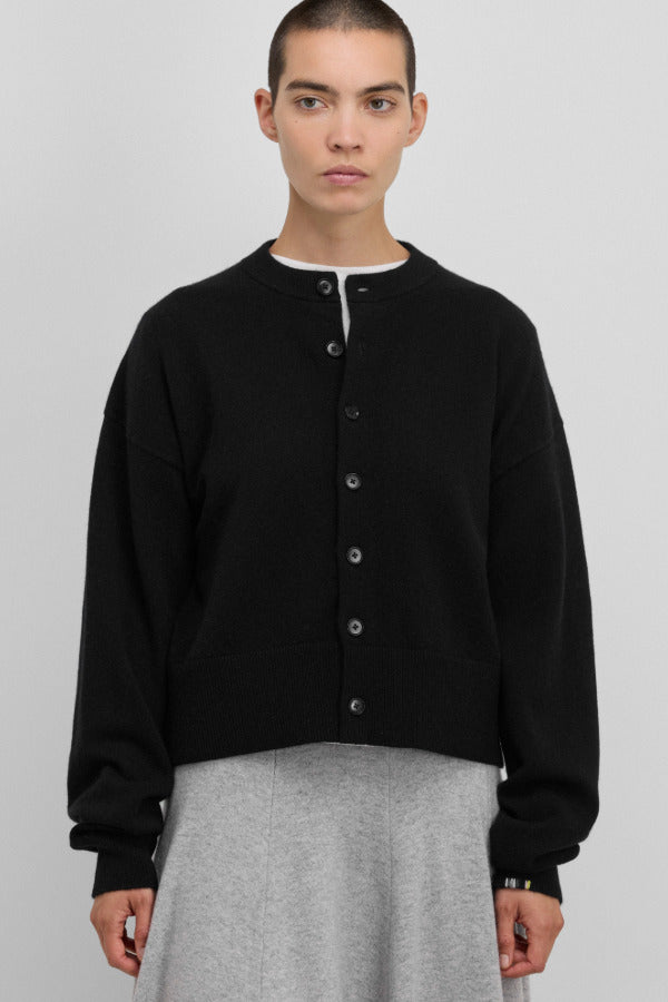 Front view of button down black cardigan on model wearing white t-shirt and grey skirt, against a white background.