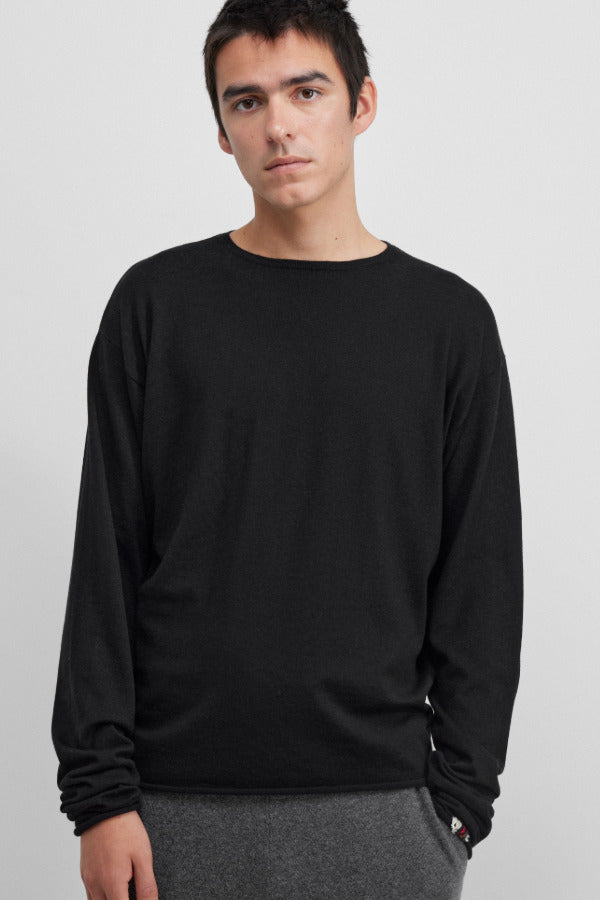 Front view of raven aries sweater on dark-haired model wearing black trousers, against  white background.