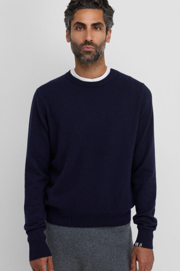 Front view of raven be classic sweater on dark-haired model wearing a white t-shirt underneath and grey trousers, against a white background.