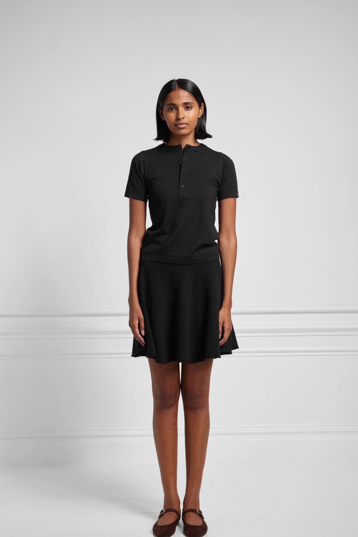 Front view of raven girl skirt on black haired model wearing short sleeve black henley and maroon mary janes.