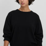 Front view of raven jewel sweater on dark-haired model wearing grey trousers, against white background.