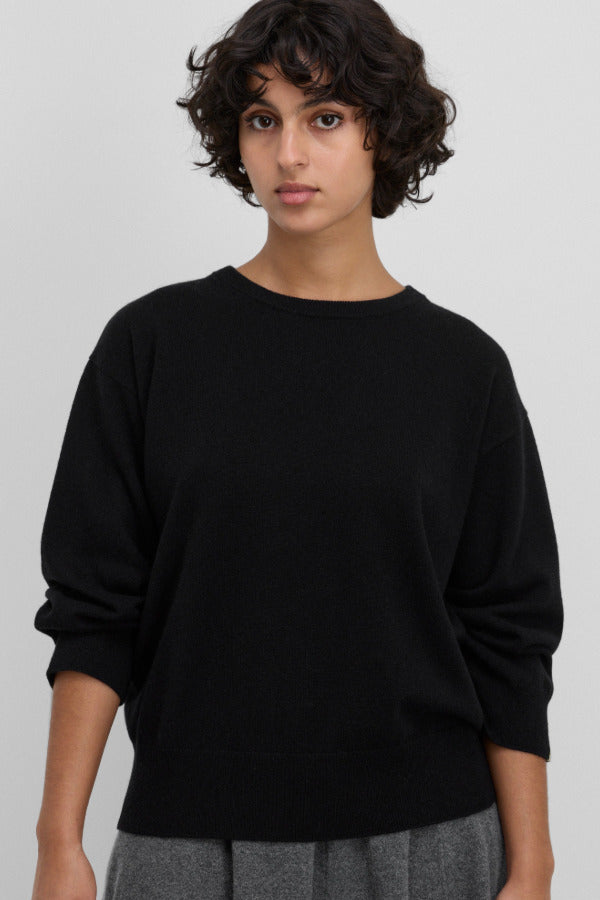 Front view of raven jewel sweater on dark-haired model wearing grey trousers, against white background.