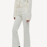 Side slanted view of white bronte jacket on model wearing white pants and boots, against a white background.