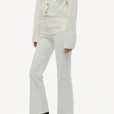 Side slanted view of white bronte jacket on model wearing white pants and boots, against a white background.