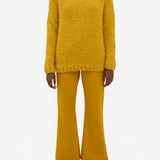 Front view of golden birch cashmere lawrence sweater on. model wearing yellow pants and sneakers, against a white background.
