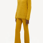 Side view of golden birch cashmere lawrence sweater on model wearing yellow pants and sneakers, against a white background.
