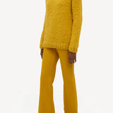 Side view of golden birch cashmere lawrence sweater on model wearing yellow pants and sneakers, against a white background.