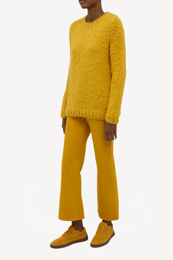 Side view of golden birch cashmere lawrence sweater on model wearing yellow pants and sneakers, against a white background.